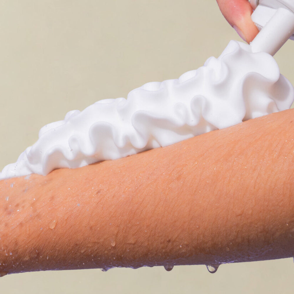 Application de la gel douche moussant Sundae Body sur le bras, fond beige